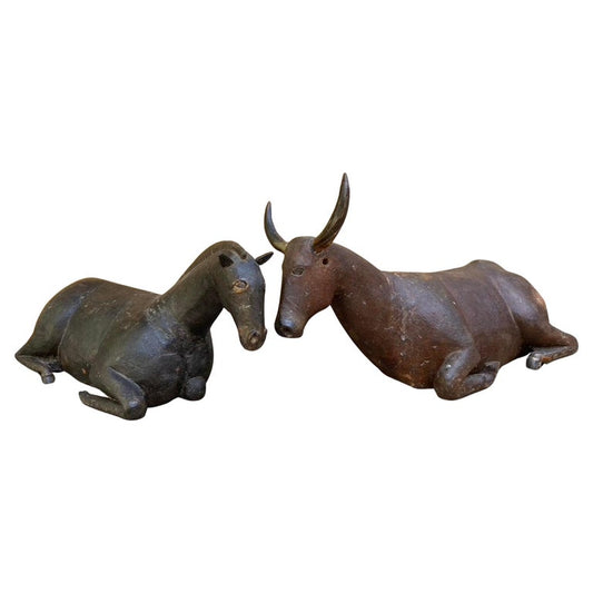 Pair of 19th century Guatemalan carved wooden nativity animals, depicting a recumbent horse and ox. Both figures retain traces of their original polychrome - the horse in deep, worn black and the ox in a warm reddish-brown with applied horn. Folk-carved with charmingly simplified anatomical details, these animals would have accompanied a large creche ensemble, reflecting the devotional artistry and rustic craftsmanship of rural Guatemala in the 1800s. Lovely patina throughout both animals. Horse hair tail